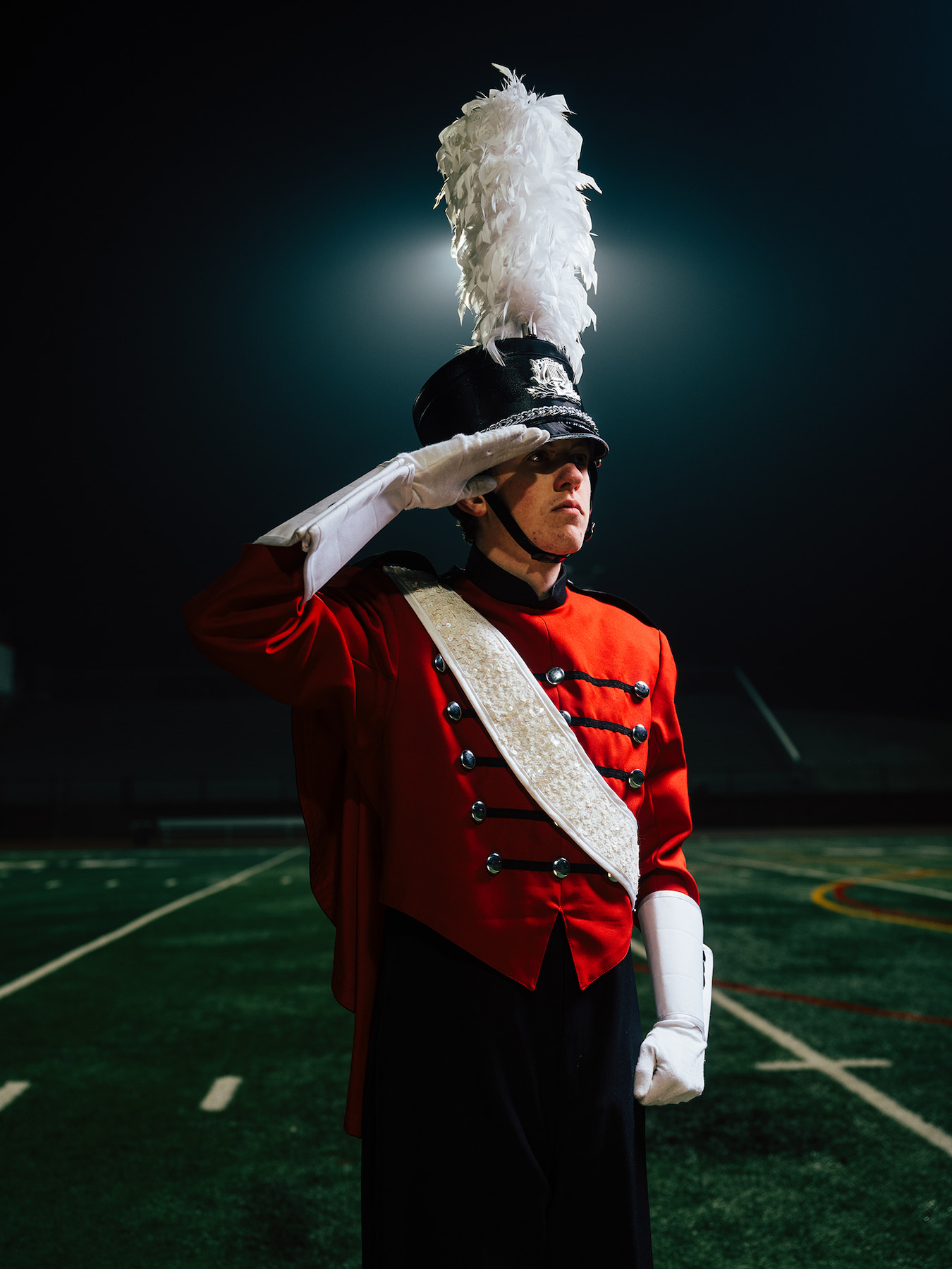High school senior in marching band uniform saluting on the football field at night